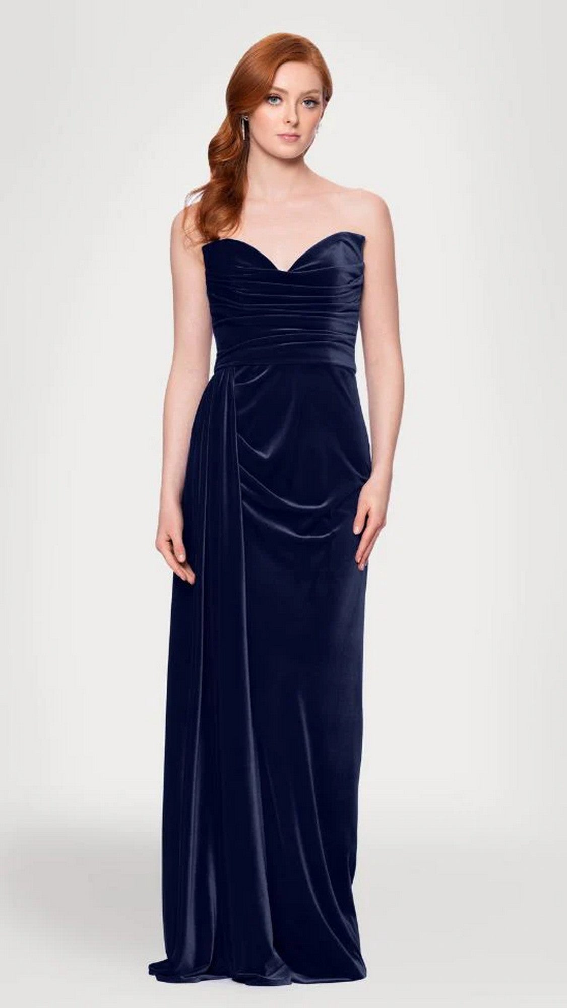 A woman models the Blondie Nites 5138BN Long Prom Dress—strapless velvet with a sweetheart neckline, floor-length sash, and elegant side draping—standing against a plain light background.